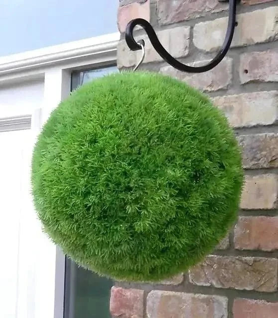 Topiary Moss: vibrant green spherical moss ball on black hook against brick wall